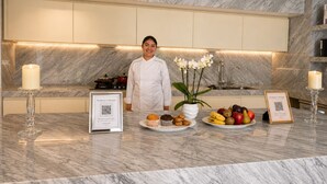 Una cucina moderna con piani di lavoro in marmo, uno chef in piedi e un espositore con frutta e muffin.