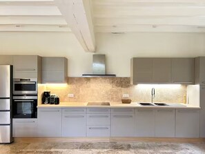 A modern kitchen with built-in appliances, a large island, and a stainless steel sink. - Magnanerie du manoir de Beauregard (Véretz)