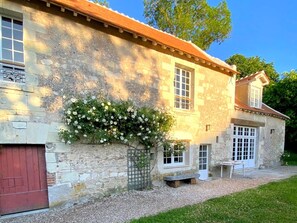 A stone building with a red door, a window with a grid pattern, and a bench outside. - Magnanerie du manoir de Beauregard (Véretz)