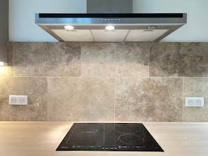 Cozinha equipada com cooktop por indução, coifa de aço inoxidável e painel de azulejos.