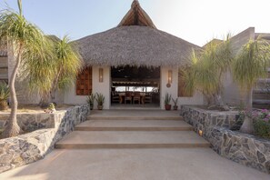 A building with a thatched roof, stone steps leading to a covered entrance, and potted plants around. - Ventana al Paraíso Oceanfront Villa (Bajos de Chila)
