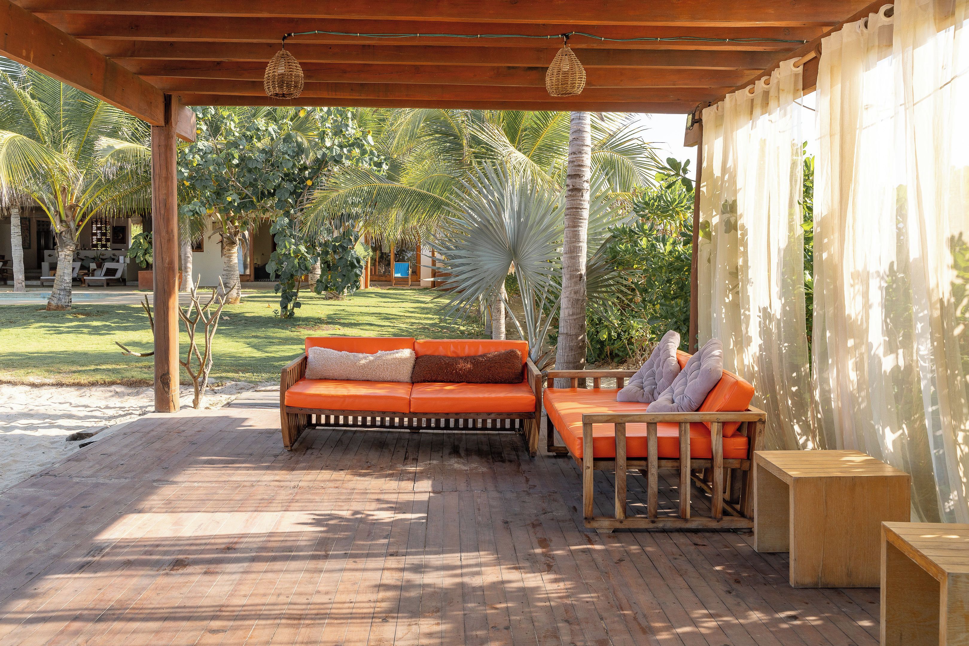 A wooden deck with a sofa and a table, surrounded by palm trees and a building in the background.