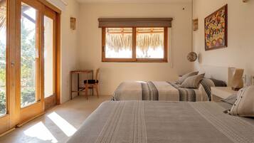Un dormitorio con dos camas, una silla, un ventanal con tejado de paja y un cuadro en la pared.