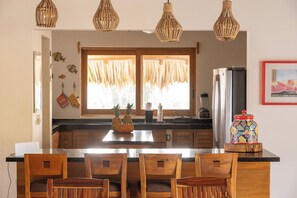 A kitchen with a central island, wooden chairs, a refrigerator, and a window with curtains.