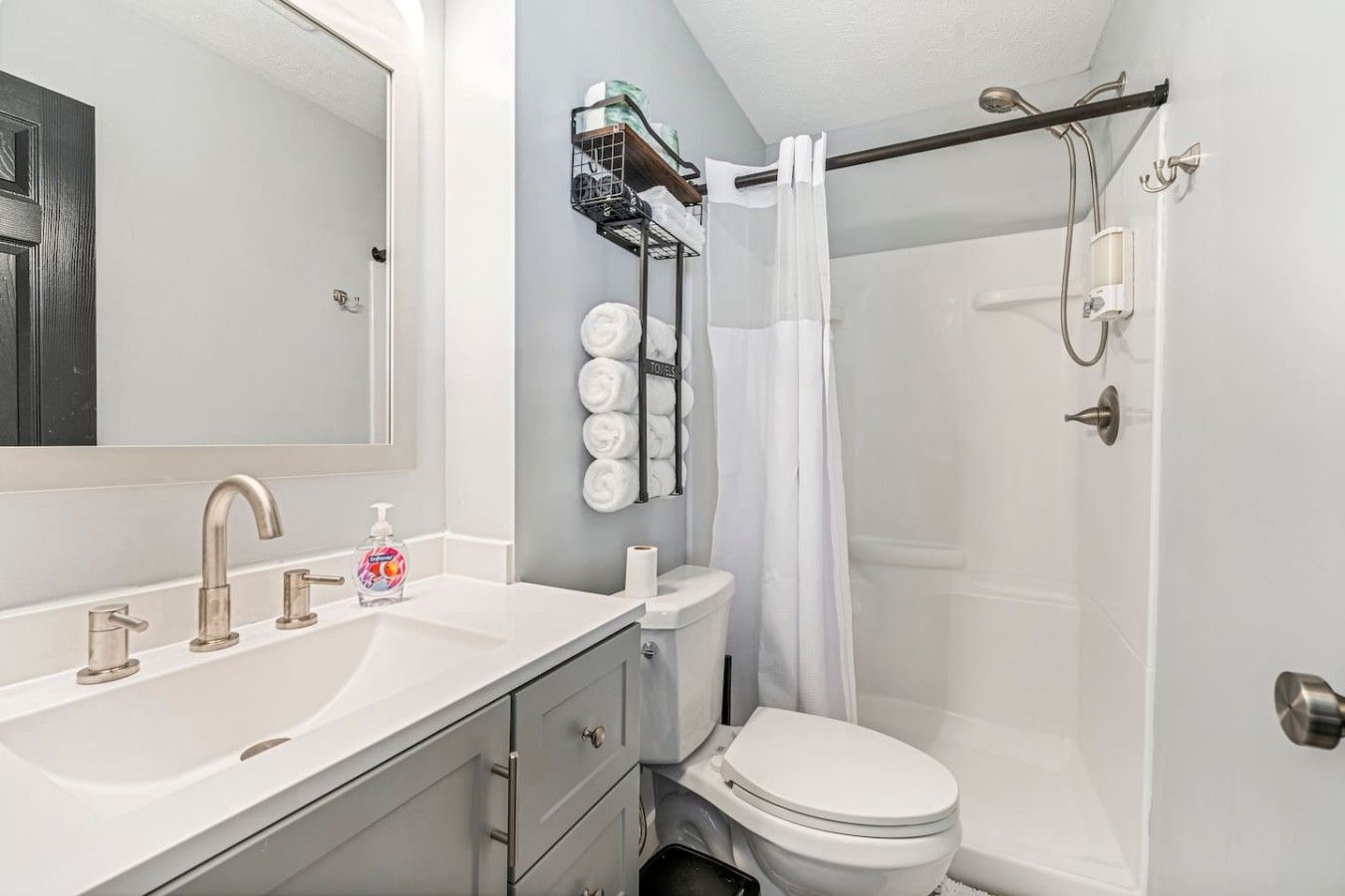 Un baño con un lavamanos blanco, un inodoro, una ducha con puerta de cristal y un perchero con toallas.