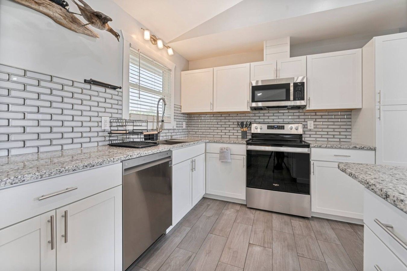 A modern kitchen with white cabinetry, a stainless steel microwave, and a built-in oven.