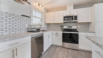 A modern kitchen with white cabinetry, a stainless steel microwave, and a built-in oven.