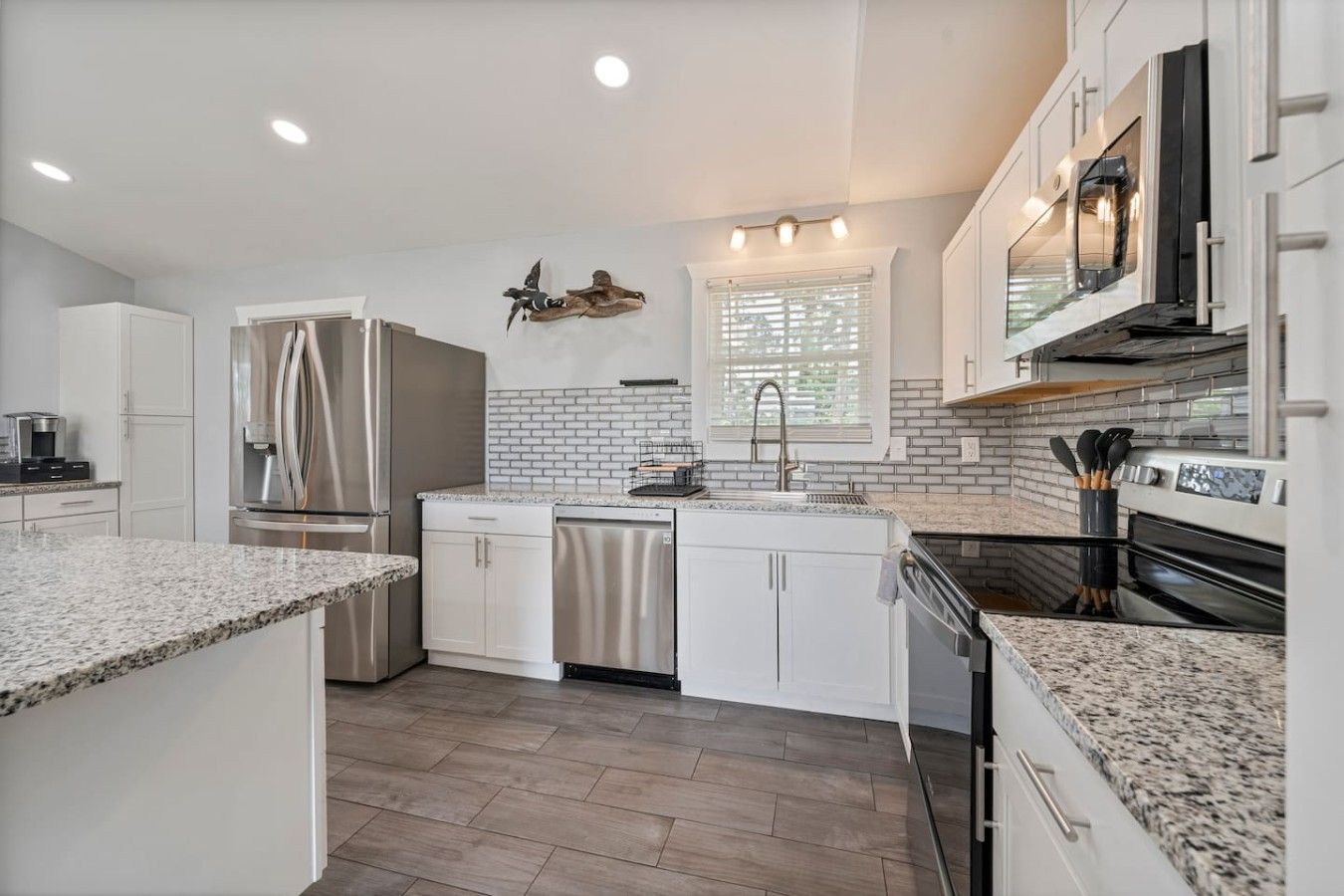 A modern kitchen with stainless steel appliances, white cabinetry, and a granite countertop.