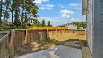 Un jardin avec une clôture en bois, une terrasse en béton et une maison en arrière-plan.