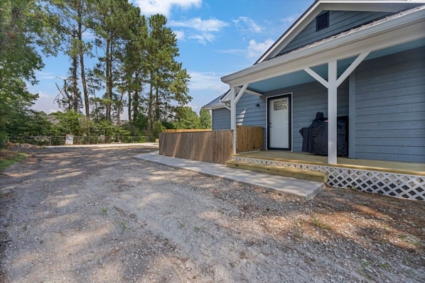 A single-story house with a porch, a front door, and a driveway leading to a gravel area.
