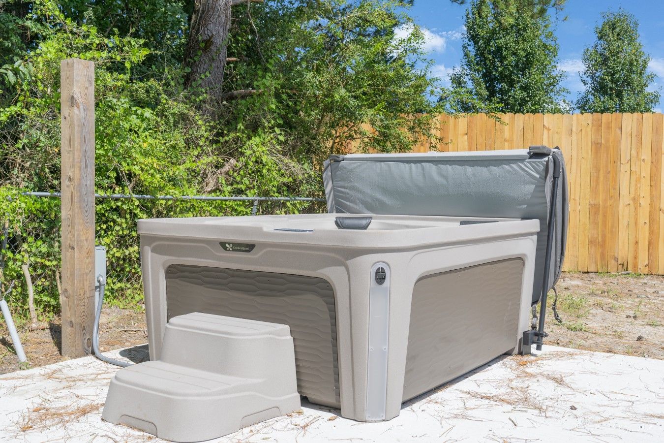 Un jacuzzi exterior con un escalón para facilitar el acceso, rodeado por una valla de madera y follaje.
