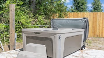 Un jacuzzi exterior con un escalón para facilitar el acceso, rodeado por una valla de madera y follaje.