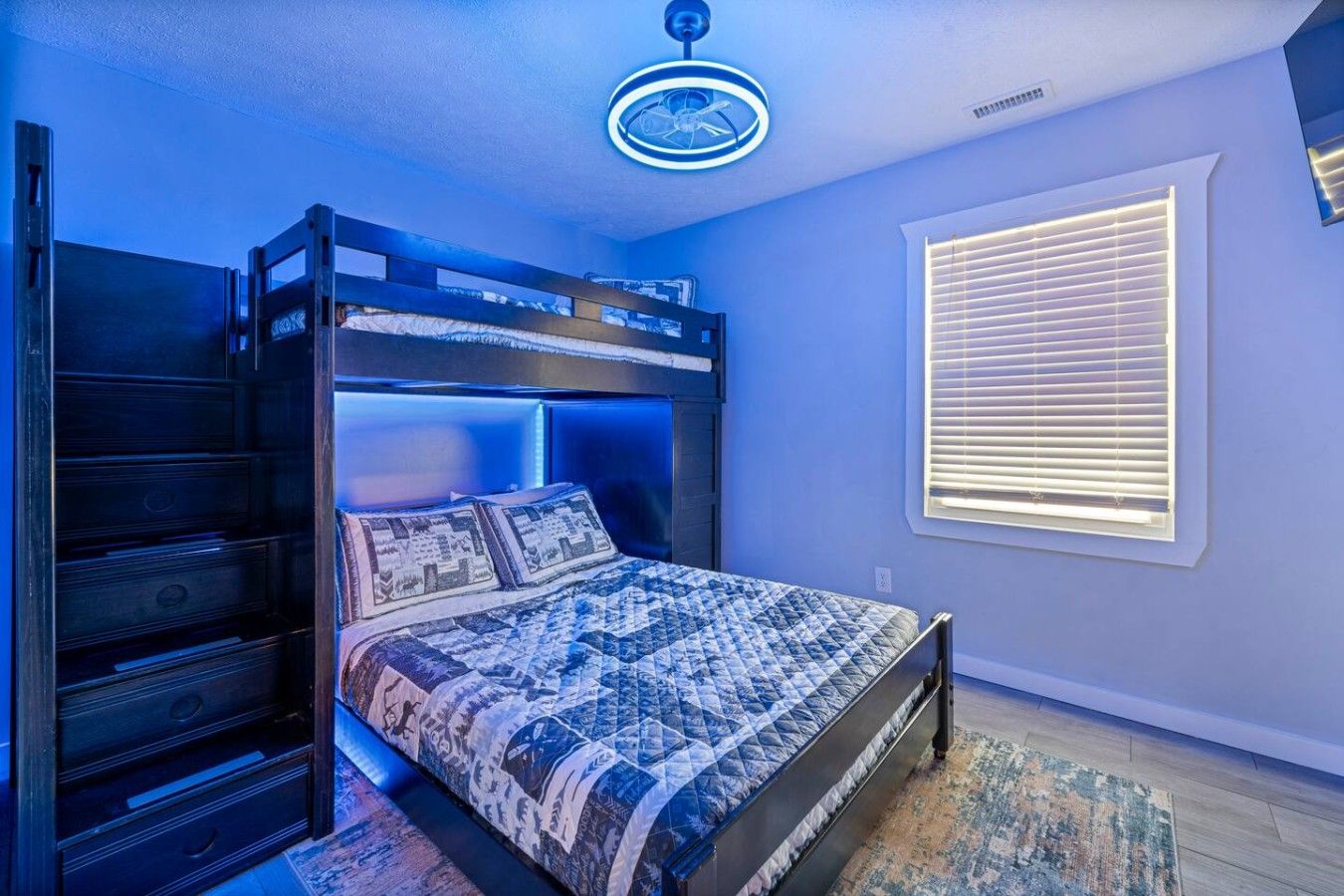 Un dormitorio con una cama litera, una mesita de noche, una ventana con persianas y un ventilador de techo.