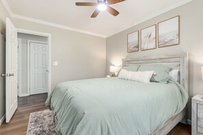 Ein Schlafzimmer mit einem Bett, einem Deckenventilator, einem Nachttisch und einer Tür.