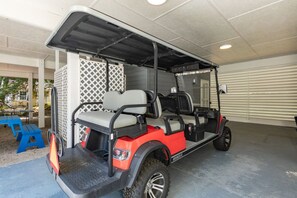 Ein Golfwagen steht in einem überdachten Parkbereich, vor dem sich ein Tisch und Stühle befinden.