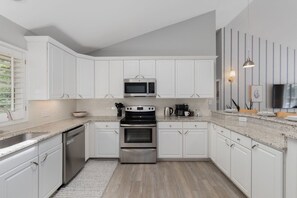 Cozinha moderna com armários brancos, eletrodomésticos de aço inoxidável e bancada de granito.
