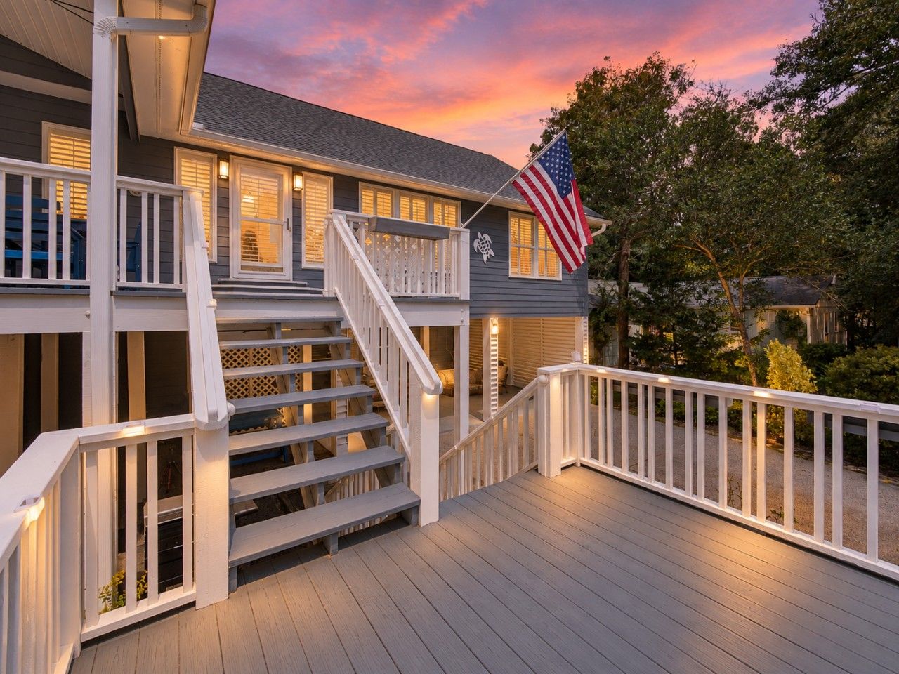 A two-story house with a wooden deck, a staircase, and an American flag.