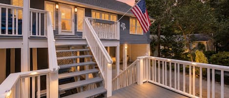 A two-story house with a wooden deck, a staircase, and an American flag.