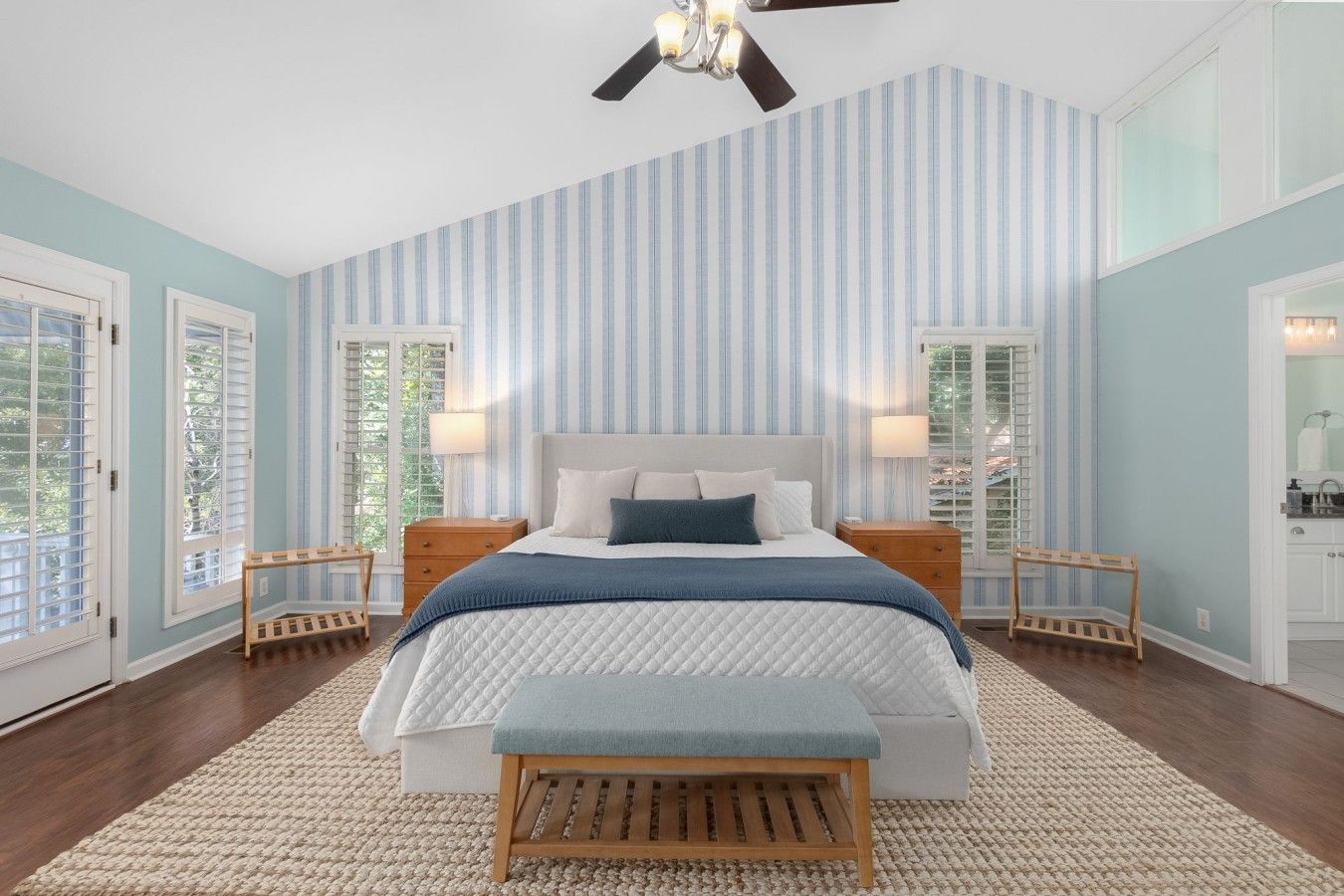 Ein Schlafzimmer mit einem großen Bett, zwei Nachttischen, einem Deckenventilator und Blick durch das Fenster.