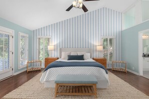 Ein Schlafzimmer mit einem großen Bett, zwei Nachttischen, einem Deckenventilator und Blick durch das Fenster.