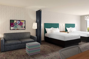 A hotel room with a gray sofa, two beds with green headboards, a colorful abstract painting, and a patterned carpet. - Home2 Suites by Hilton Wheat Ridge Golden (Wheat Ridge)