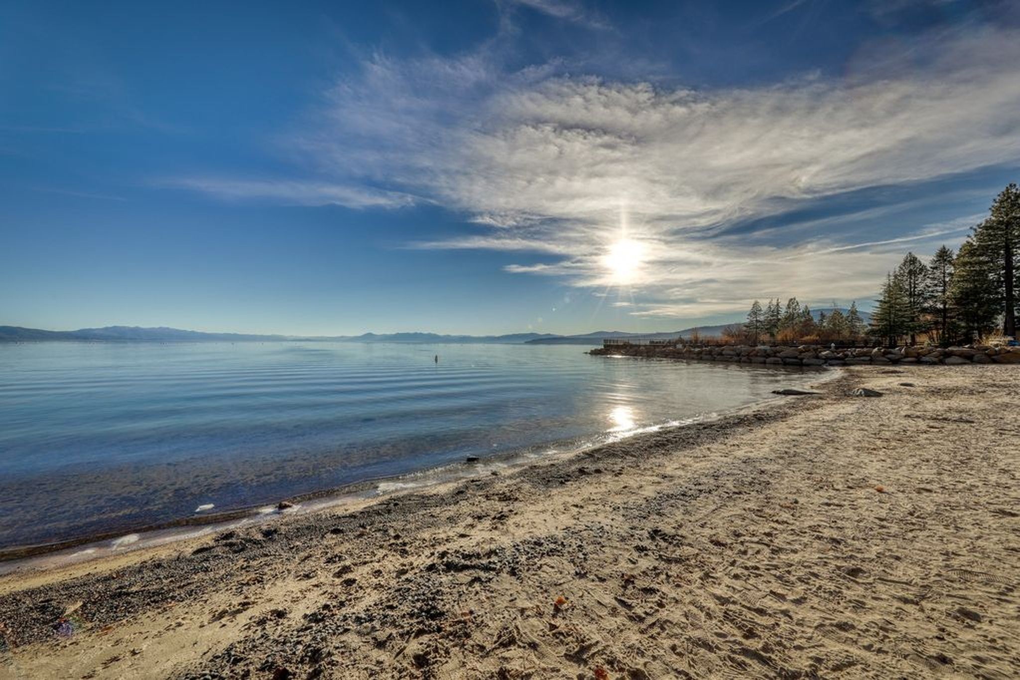 A beach with a clear sky, calm water, and a rocky shoreline.