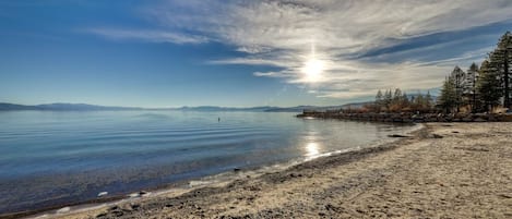 A beach with a clear sky, calm water, and a rocky shoreline.