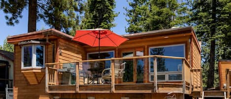 A wooden cabin with a balcony, a red umbrella, and a view of the surrounding forest.