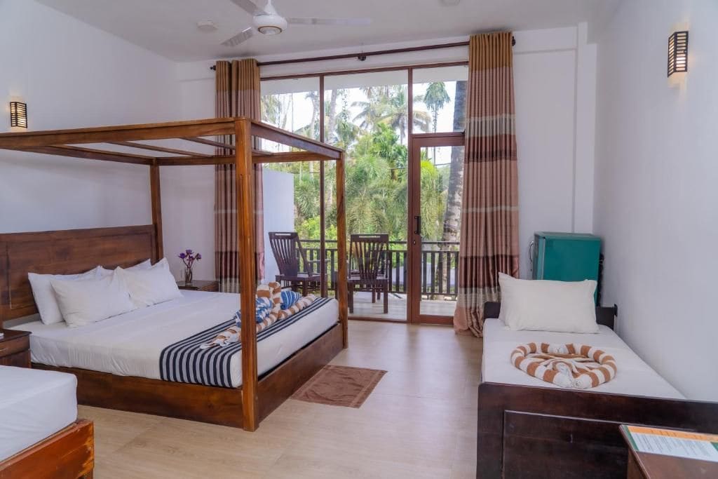 A hotel room with a large bed, a smaller bed, a desk, and a balcony with a view of palm trees.