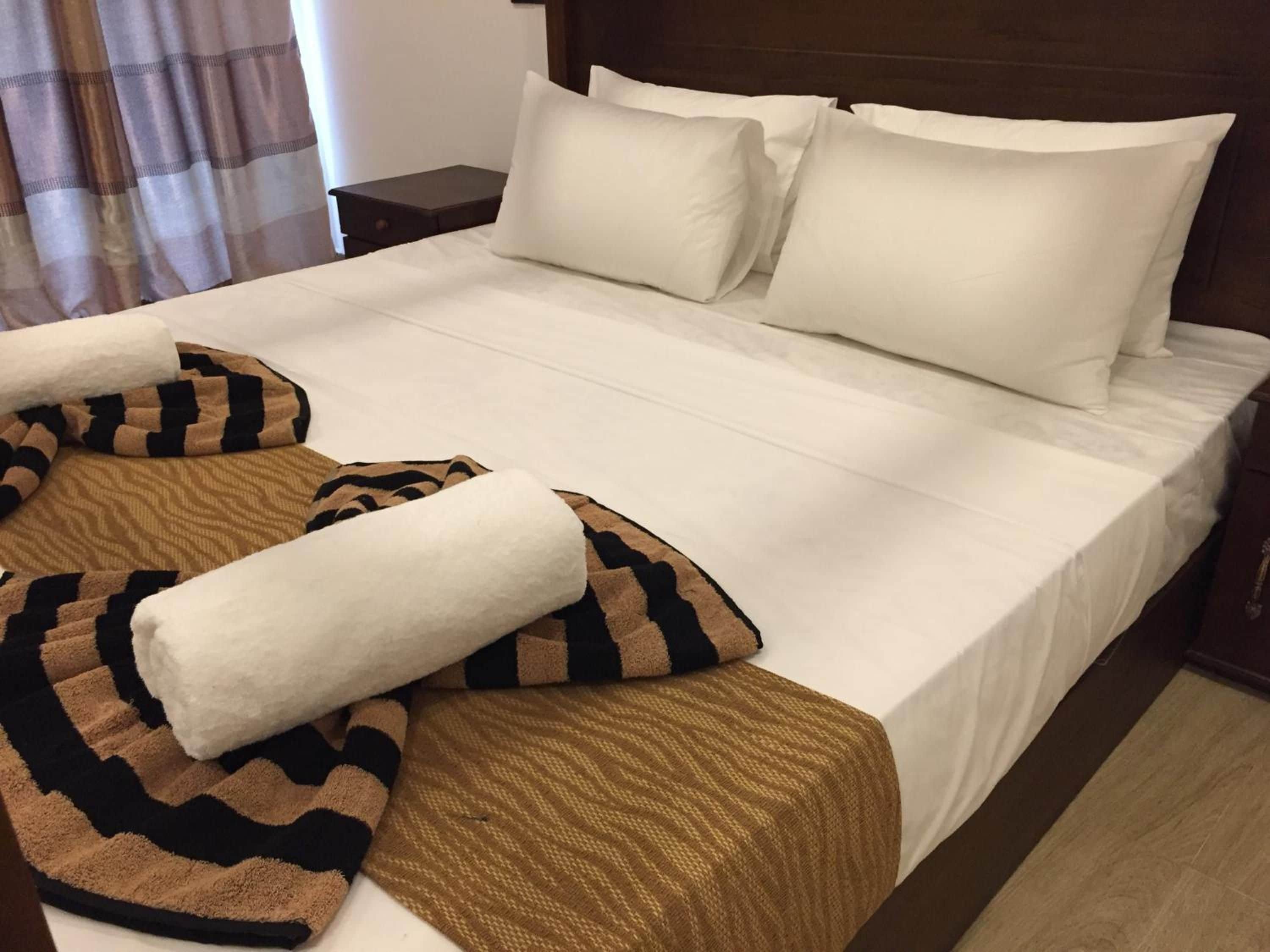 Una cama bien tendida con sábanas blancas y un plaid estampado.
