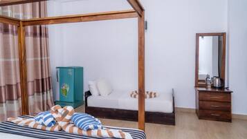 A bedroom with a four-poster bed, a wooden dresser, a mirror, and a green cabinet.