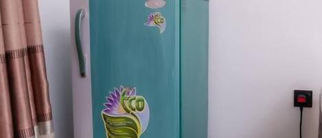 Un refrigerador color turquesa con una pegatina, conectado a un enchufe sobre un piso de madera.