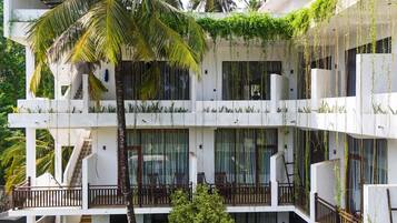 Un edificio de varios pisos con balcones, algunos con plantas, y una palmera.