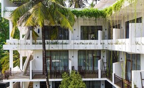 A multi-story building with balconies, some with plants, and a palm tree.