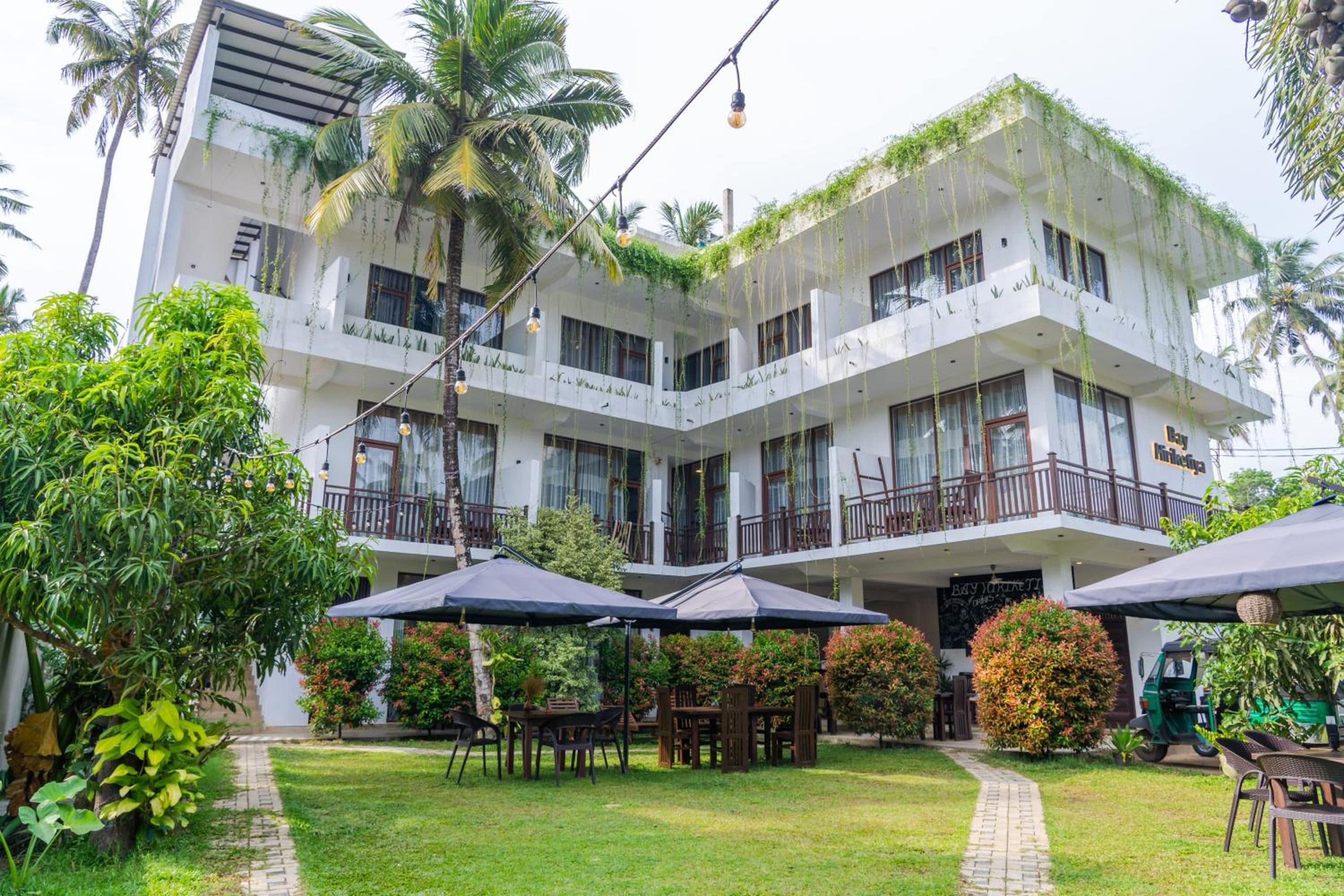 Un edificio de varios pisos con balcones, mobiliario exterior y abundante vegetación.