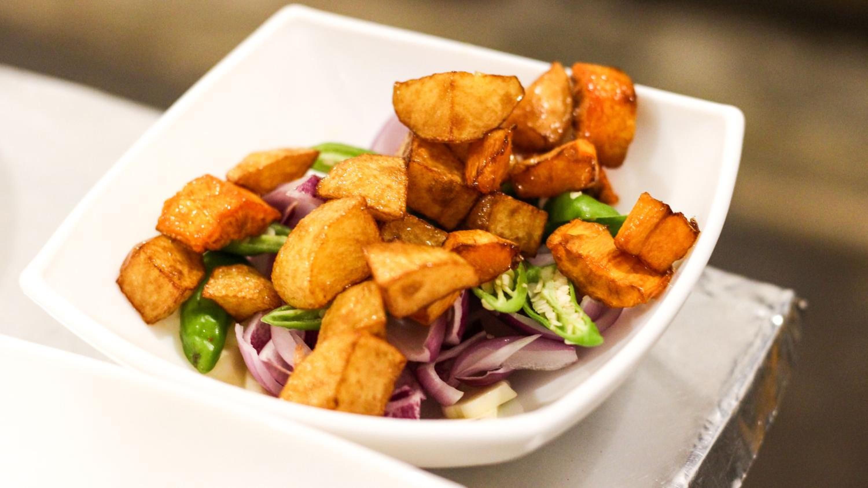 A white square plate with fried potato pieces and mixed greens.