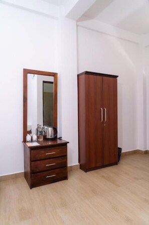 A room with a wooden wardrobe, a mirror, and a small wooden dresser.