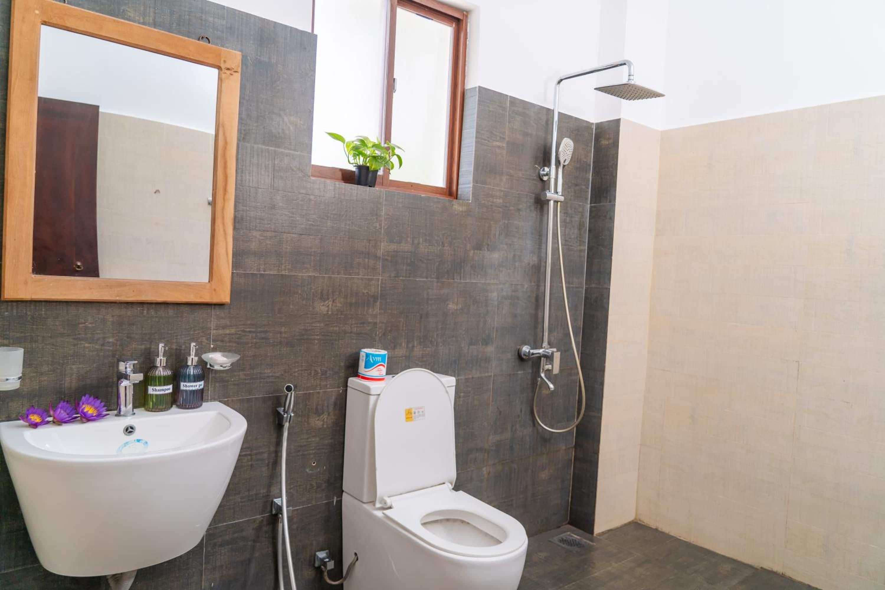 A bathroom with a white sink, a toilet, and a shower. There is a mirror above the sink and a small window above the shower.