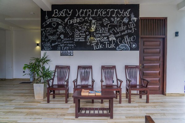 A room with a large chalkboard wall displaying a menu, wooden chairs, and a table with a book.