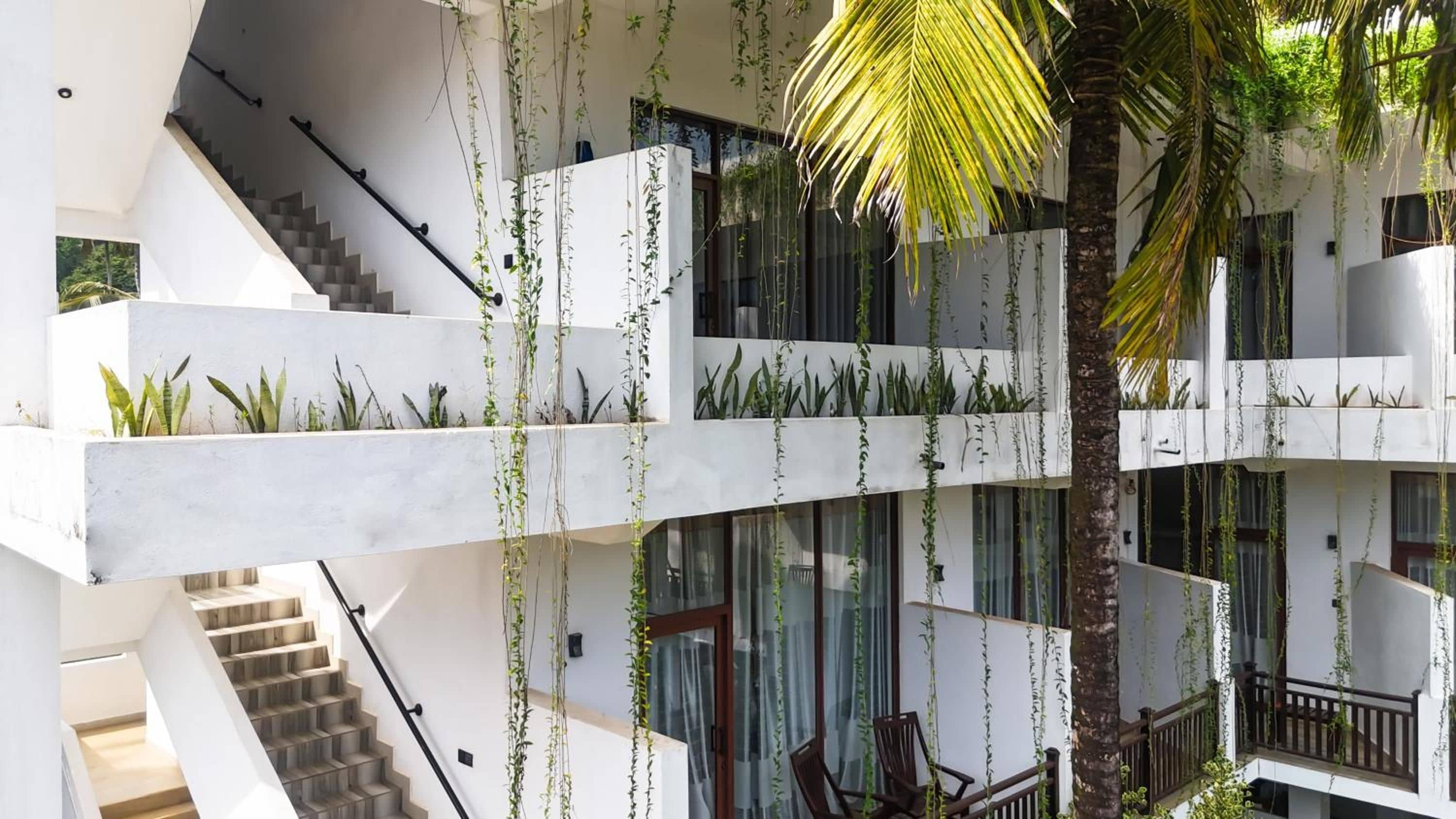 Un interior de varios niveles con escalera, barandillas de vidrio y plantas de interior.
