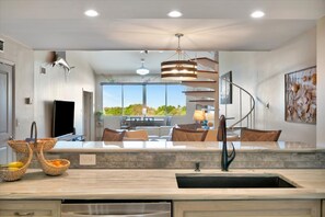 Una cocina moderna con una isla central, un área de comedor con vistas y una escalera que sube a un nivel superior.