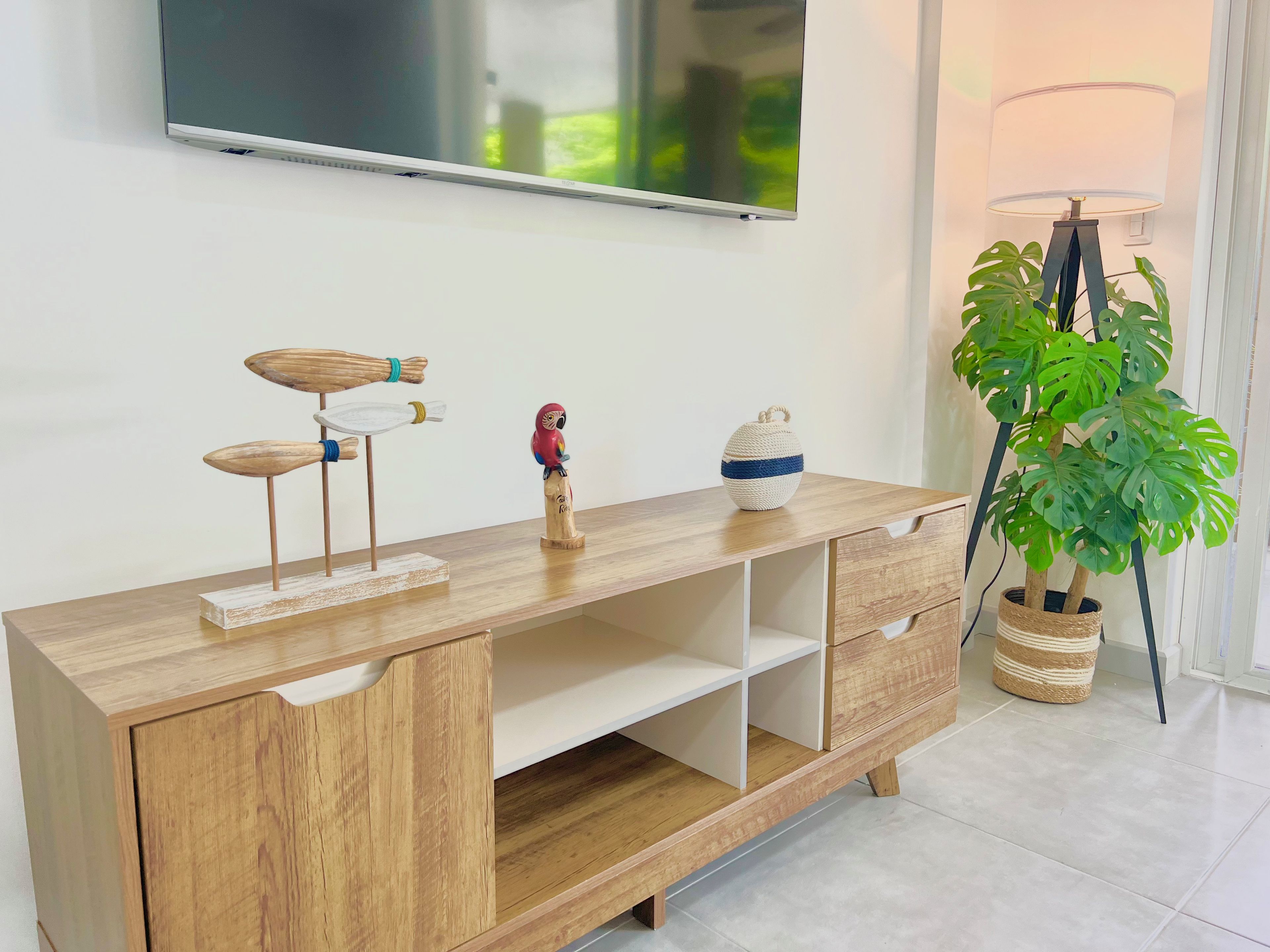 Une console en bois sur laquelle est posée une télévision à écran plat, une statuette d’oiseau décorative et un panier tressé contenant une plante.