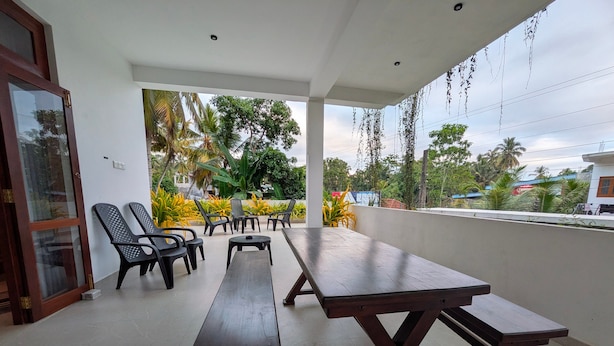 Une terrasse extérieure avec des tables et des chaises en bois, entourée de verdure et donnant sur un quartier résidentiel.