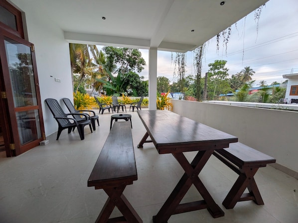 An outdoor patio with wooden tables and chairs, surrounded by greenery and overlooking a residential area.