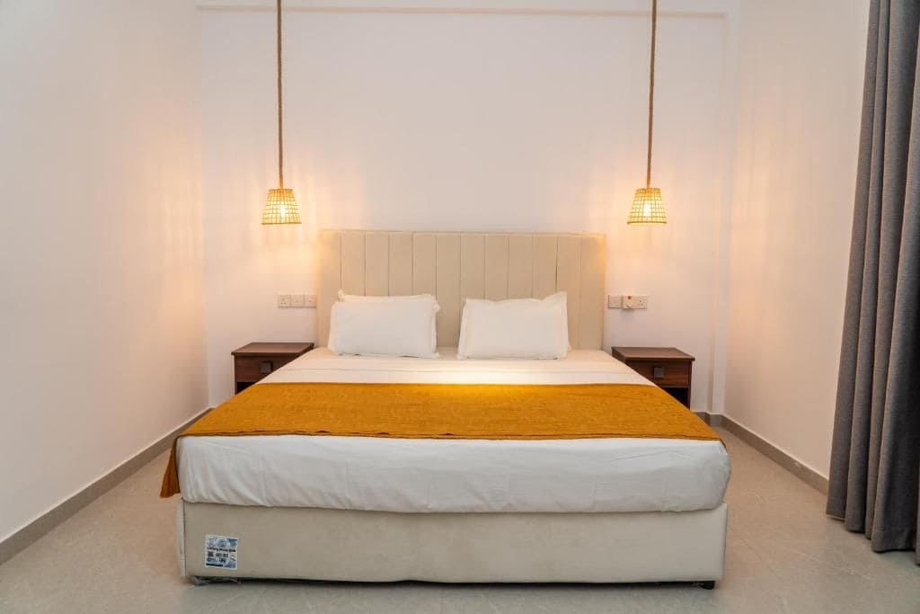 A hotel room with a bed, two bedside tables, and two hanging lamps.