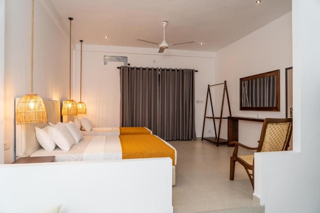 A hotel room with a bed, two bedside lamps, a ceiling fan, a window with curtains, a chair, and a painting on the wall.