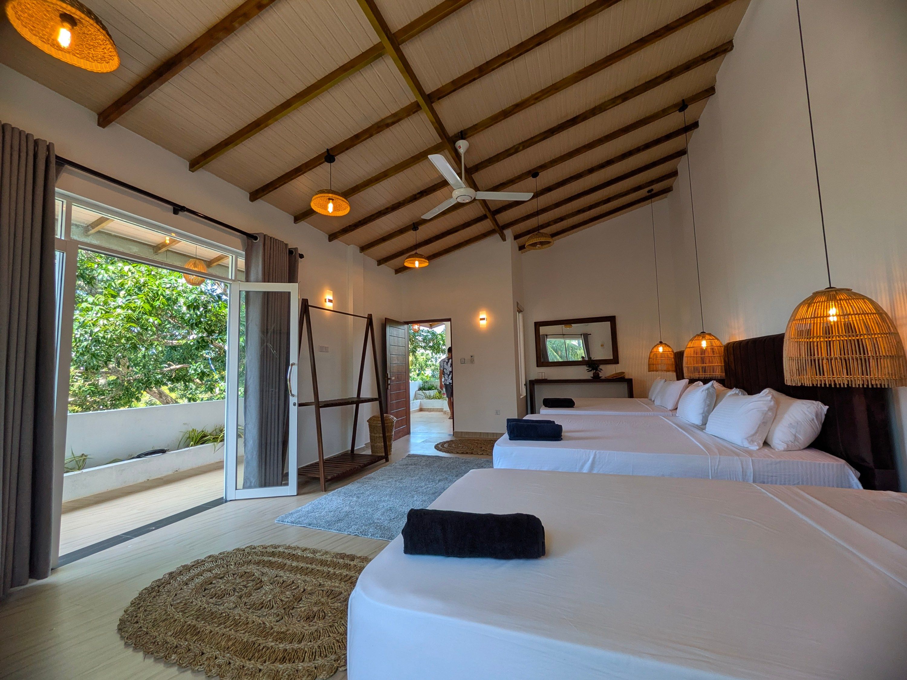 Habitación de hotel con dos camas, un ventilador de techo y un amplio ventanal con vistas a la vegetación.
