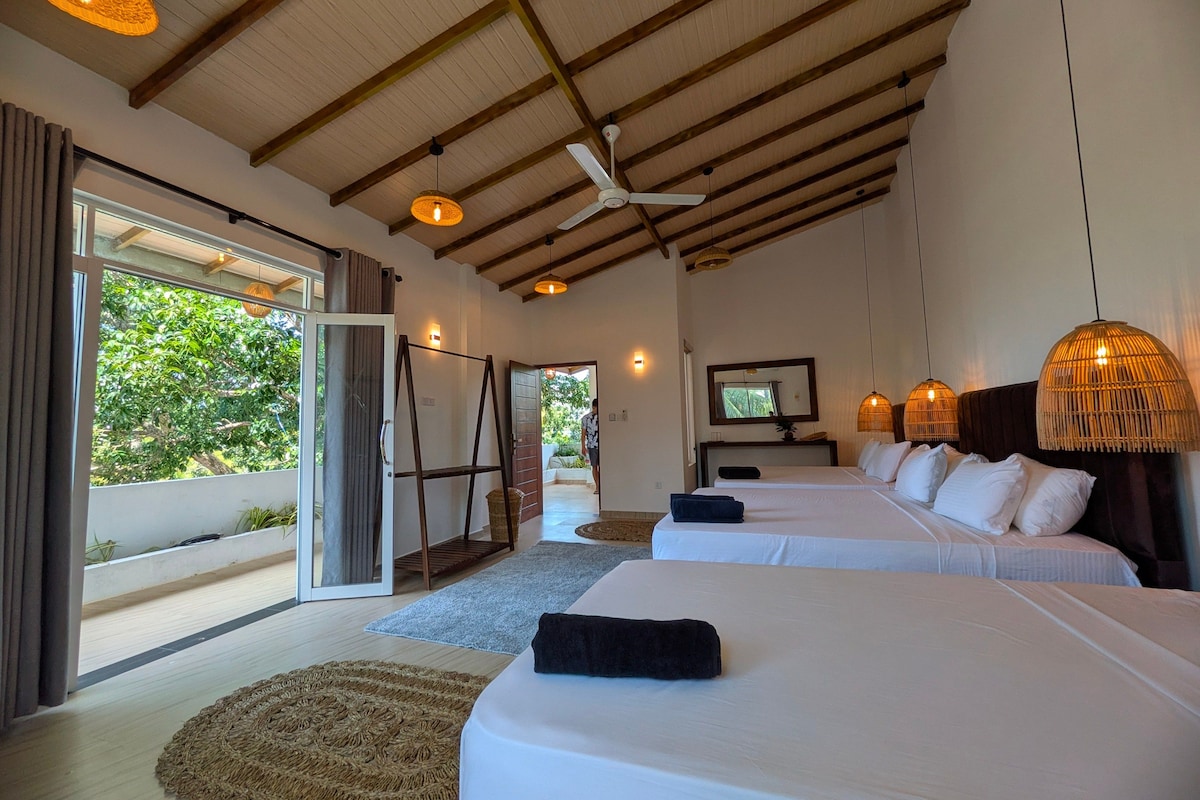 A hotel room with two beds, a ceiling fan, and a large window with a view of greenery.