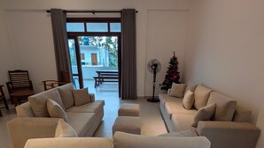 Un salon avec un ensemble de canapés, un ventilateur sur pied et un sapin de Noël.