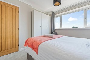 Ein Schlafzimmer mit einem Bett, einem Kleiderschrank, einem Fenster mit Vorhängen und einer Deckenleuchte.